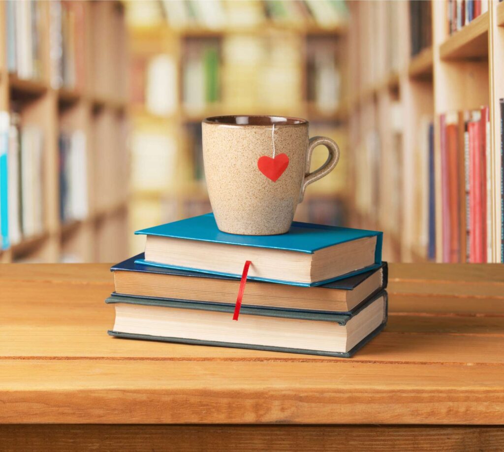 A grey mug of tea with a heart shaped tea tag sitting on top of three books